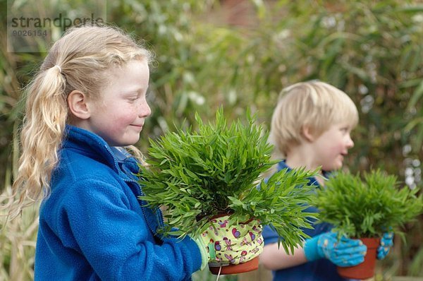 Schuljunge und Mädchen mit Pflanzen im Garten