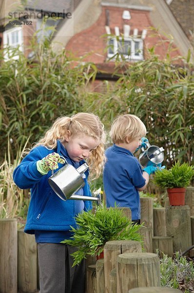 Schuljunge und -mädchen gießen Pflanzen im Garten