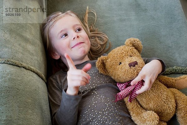 Junges Mädchen mit Teddybär auf dem Sofa liegend