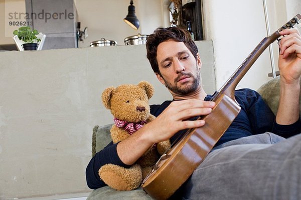 Mittlerer Erwachsener Mann  der auf dem Sofa liegt und Gitarre spielt.