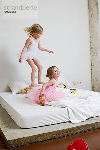 Zwei junge Schwestern als Balletttänzerinnen  die auf dem Bett spielen.