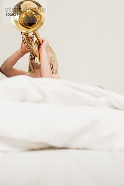 Mädchen spielt Trompete im Bett