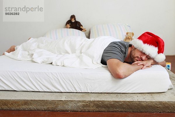 Mittlerer erwachsener Mann mit Weihnachtsmann im Bett schlafend