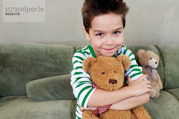 Porträt eines kleinen Jungen auf einem Sofa  der den Teddy umarmt.