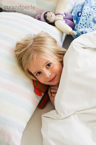 Porträt eines jungen Mädchens im Bett liegend mit Puppe