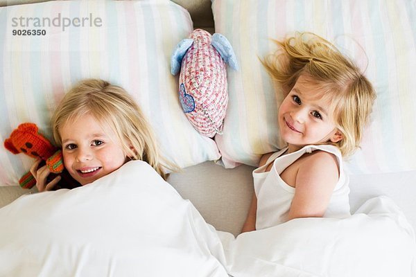 Porträt von zwei jungen Schwestern  die nebeneinander im Bett liegen.