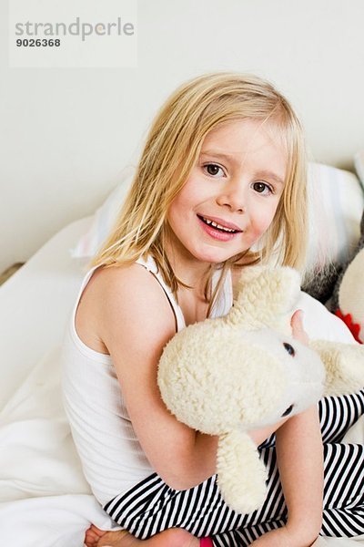 Porträt eines jungen Mädchens auf dem Bett kniend mit Plüschtier