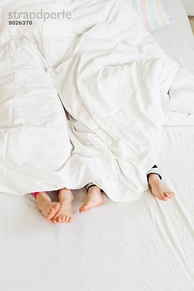 Junge Schwesternfüße aus der Bettdecke auf dem Bett herausragend