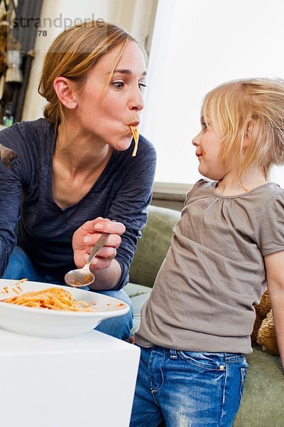 Mittlere erwachsene Mutter  die mit ihrer Tochter Spaghetti isst.