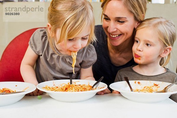 Mittlere erwachsene Mutter isst Spaghetti mit ihren beiden jungen Töchtern.