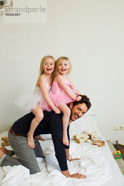 Porträt eines erwachsenen Vaters  der zwei jungen Töchtern einen Huckepack gibt.