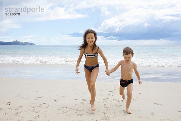 Bruder und Schwester laufen am Strand und halten sich an den Händen.