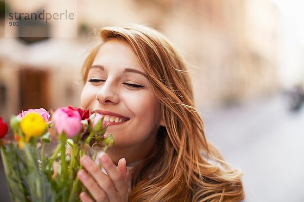 Lächelnde junge Frau  die einen Strauß Blumen riecht.