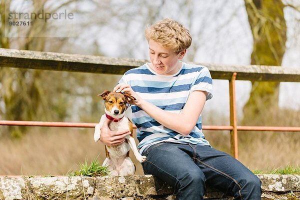 Teenager-Junge sitzt mit seinem Jack Russell Dog auf dem Steg.