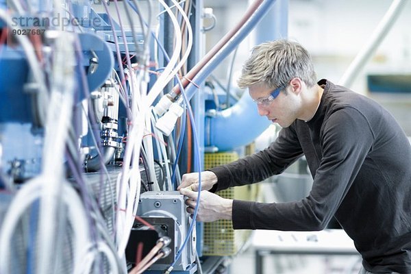 Mittlerer Erwachsener  männlicher Techniker  der die Kabel im Maschinenbaubetrieb pflegt