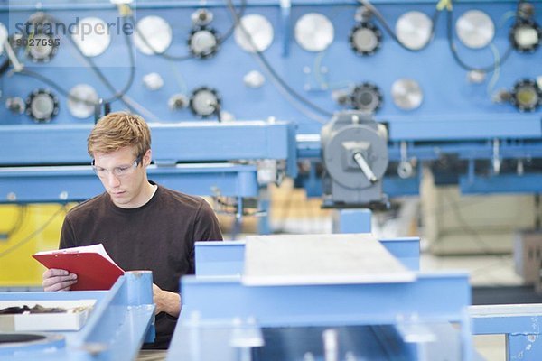 Mittlerer Erwachsener  männlicher Techniker  der den Papierkram in der Maschinenfabrik überprüft.