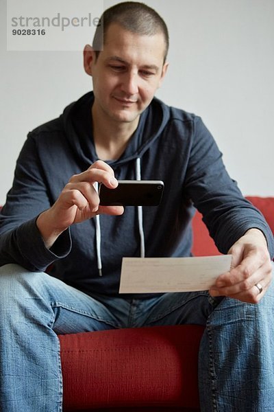 Mittlerer Erwachsener Mann auf Sofa-Fotopapier sitzend mit Smartphone