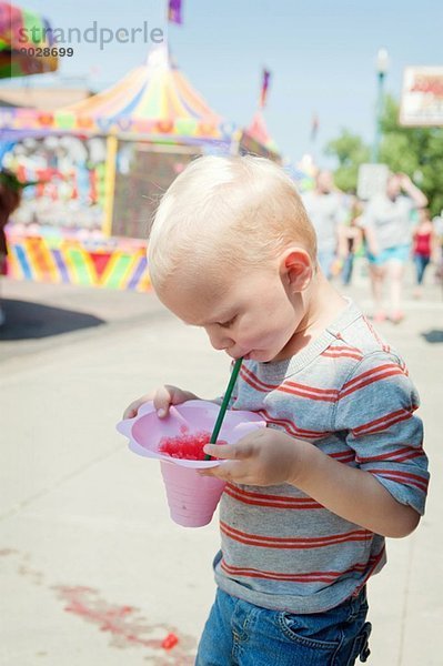 Männliches Kleinkind konzentriert sich auf Saftgetränk auf der Kirmes
