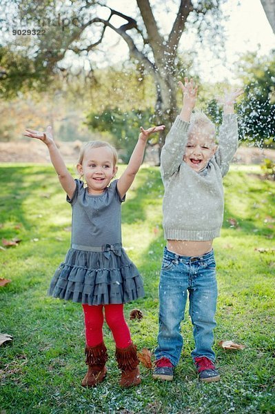 Bruder und Schwester mit erhobenen Armen  im Garten