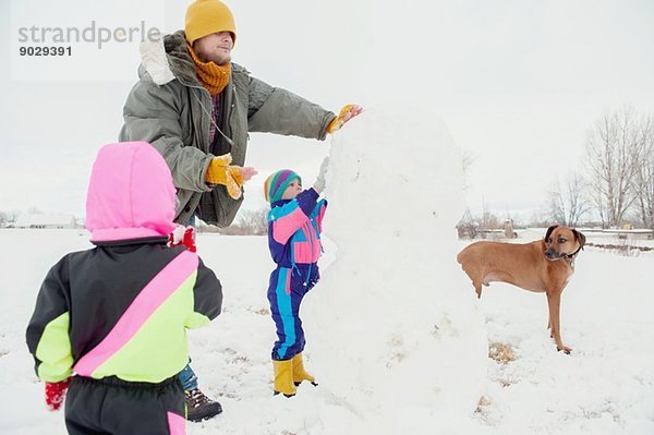 Vater und Kinder bauen Schneemann
