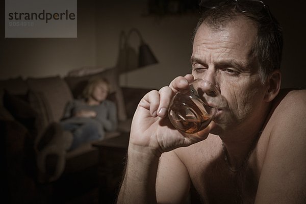 Mature man drinking  woman on sofa on background