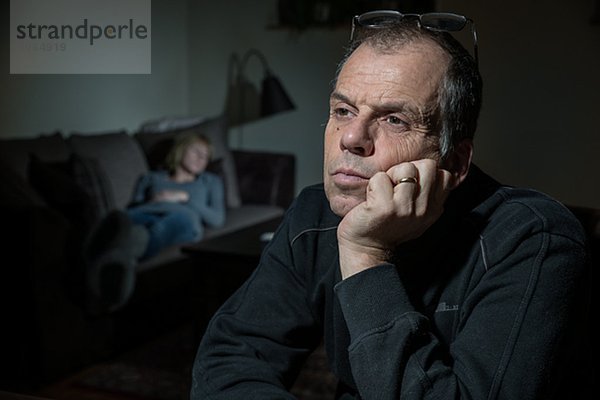 Mature man looking away  woman on sofa on background