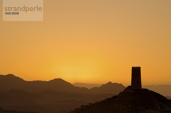 Sonnenaufgang hinter der Silhouette eines einsamen  verfallenden Wachturms am Rande der Wahiba Sands Wüste  Al Mudayrib  asch-Scharqiyya  Oman