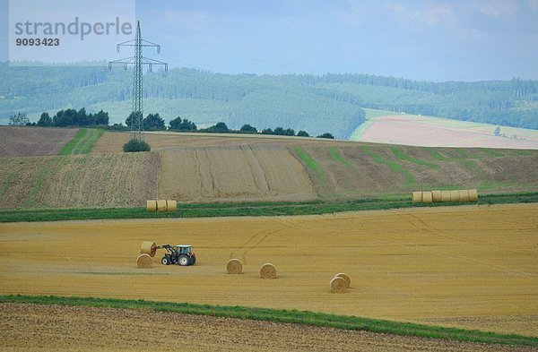Ein Traktor transportiert Strohballen auf einem abgeernteten Getreidefeld.