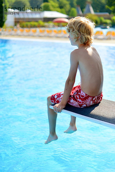 Ein Junge sitzt auf einem Sprungbrett im Freibad.