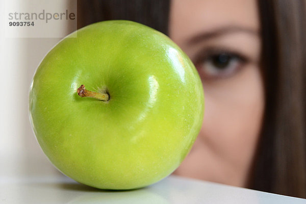 Das Gesicht einer Frau hinter einem grünen Apfel.