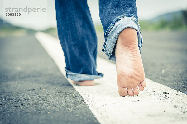 Junge Frau geht barfuß auf der Mittellinie der leeren Straße  Teilansicht