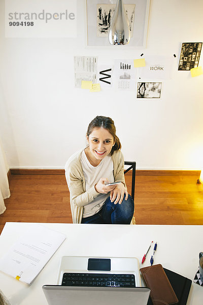 Porträt einer Frau mit Smartphone im modernen Home Office  erhöhte Ansicht