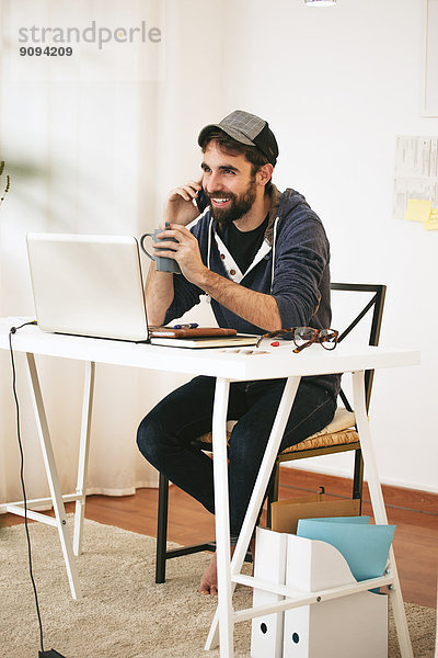 Porträt eines Mannes beim Telefonieren mit dem Smartphone im modernen Home Office