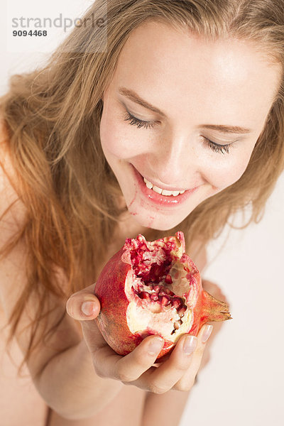 Porträt einer lächelnden jungen Frau beim Granatapfelessen