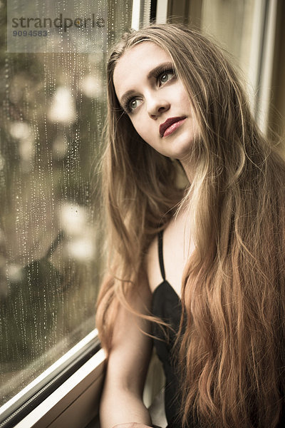 Porträt einer jungen Frau beim Blick durchs Fenster