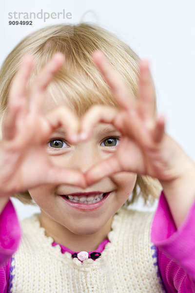 Porträt eines kleinen Mädchens  das das Herz mit den Fingern formt.