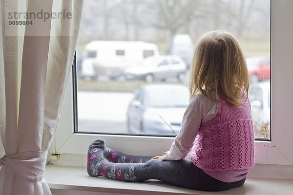 Kleines Mädchen sitzt auf der Fensterbank und schaut aus dem Fenster.