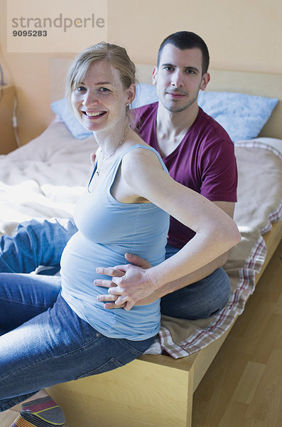 Ein Paar erwartet ein Baby  das zu Hause auf dem Bett sitzt.