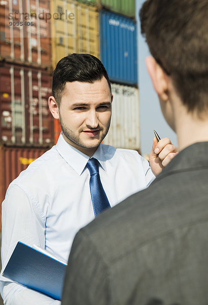 Porträt eines Geschäftsmannes im Gespräch mit einem Teenager am Containerterminal