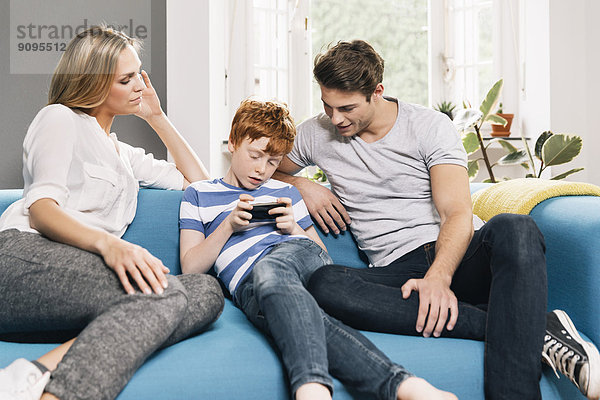 Junge Familie sitzt auf der Couch und schaut auf das Smartphone