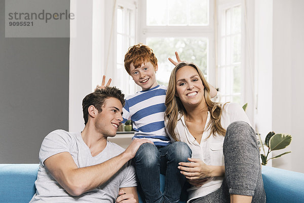 Porträt einer jungen Familie  die auf der Couch im Wohnzimmer sitzt.