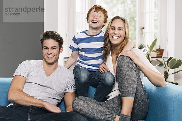 Porträt einer lachenden jungen Familie  die auf ihrer Couch im Wohnzimmer sitzt.