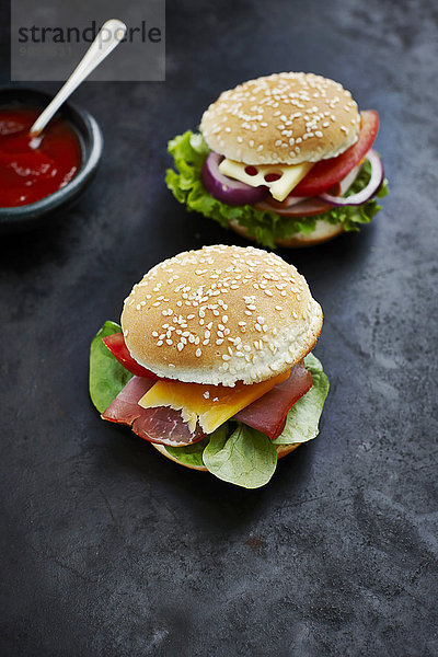 Zwei zubereitete Burger  Senf und Ketchup auf dunklem Grund