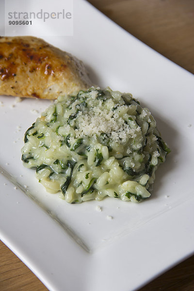 Spinat-Gorgonzola-Risotto mit Parmesan und gebratener Hähnchenbrust auf einem Teller