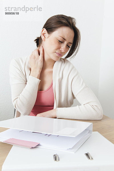 Junge Frau mit Nackenschmerzen zu Hause mit Schreibtischarbeit