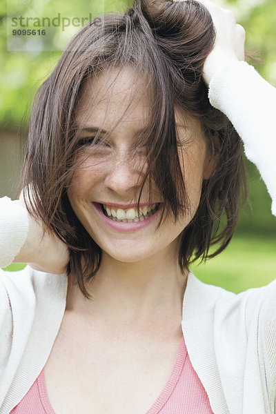 Porträt einer lächelnden jungen Frau mit Händen im Haar