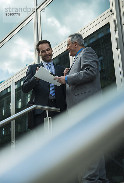 Zwei Geschäftsleute besprechen Dokumente außerhalb des Bürogebäudes
