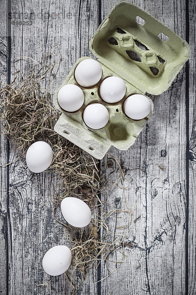 Eierkarton mit weißen Eiern und Heu auf Holzbrettern  Ansicht von oben