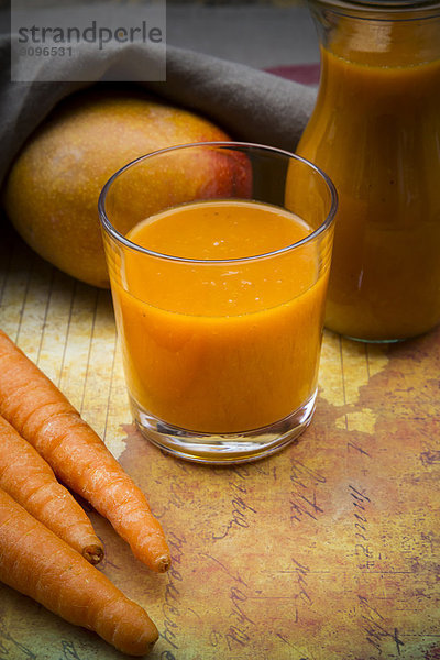 Glass of mango carrot smoothie  carrots and mango on paper