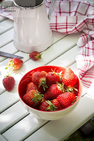 Schale mit Erdbeeren  Küchentuch und Glas auf weißem Holz
